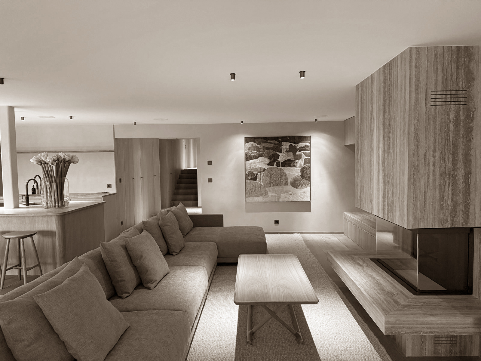 This living space embodies refined simplicity. A long, low-profile sofa with clean lines invites relaxation, while the natural wood textures—from the cabinetry to the minimalist coffee table and fireplace cladding—create warmth and harmony. Neutral tones and subtle lighting emphasize the calm, uncluttered ambiance.